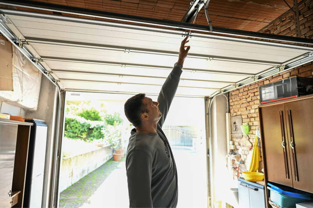 A man reaches up to a garage door, focusing on the track repair process.